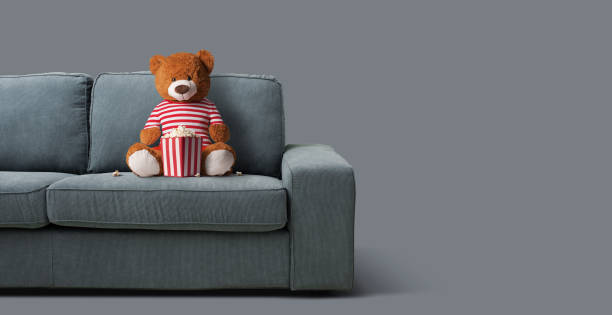 Teddy bear sitting on the couch and watching movies at home