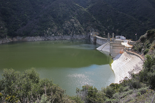 The reflective high water of the Morris Dam against its concrete crest complex as seen from Highway 39 north of Azusa, California.