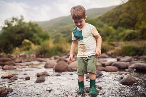 Happy little boy playing in the shallow mountain river.