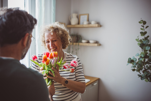 Mature man giving bouquet of tulips to his wife. They are happy and cheerful.