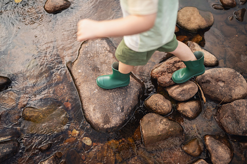 An unrecognizable boy crossing natural stepping stones over the shallow mountain river.