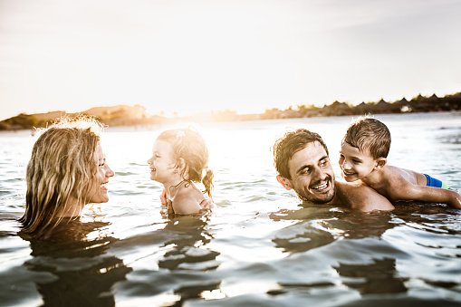 Happy parents and their small kids having fun in sea during summer day. Copy space.