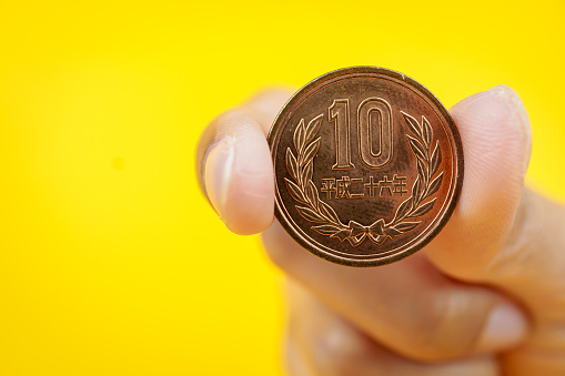Woman hand holding Japanese Yen coin on yellow background.
