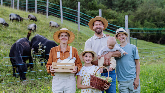 Portrait of farmer family holding harvest basket full of fresh vegetables, standing in front of paddock. Concept of multigenerational and family farming.