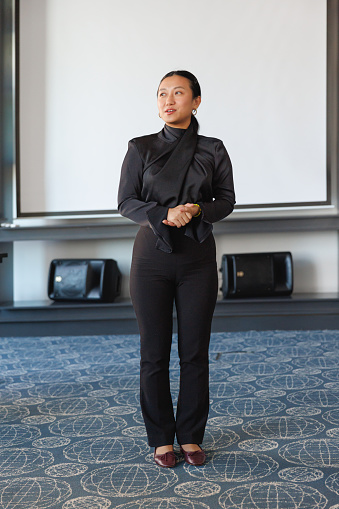 Millennial Asian businesswoman standing in front of the meeting and giving presentation