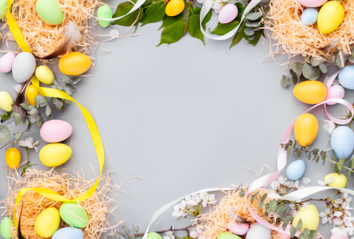 Stylish background with colorful easter eggs isolated on gray background with green eucalyptus plants. Flat lay, top view, mockup with copy space, overhead, template.
