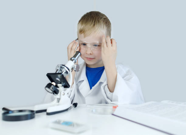 istock Child chemist. Teacher shows a visual experiment. A science mentor teaches an experimental approach. Microscope, petri dish, pipettes, books. Practical work in chemistry or physics. Laboratory work 2062666996