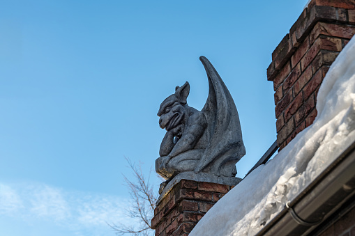 Gypsum Gargoyle sits on the roof against the blue sky. Sculpture on the roof of a building in Yaroslavl. The sculpture is located on the roof of one of the old residential buildings in city of Yaroslavl. The sculpture can be observed walking along the street. Access to this building is not fenced and completely free.