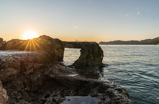 Seascape, sunset. In the foreground is a huge stone with a large hole. Through the stone view of the sea. The rays of the setting sun.