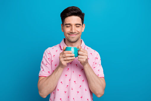 Photo of nice satisfied young man closed eyes smell fresh aroma coffee isolated on blue color background.