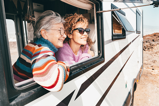 Two smiling women traveling in camper van motor home looking out of the window. Caucasian couple of females enjoying lifestyle, travel, vacation, freedom