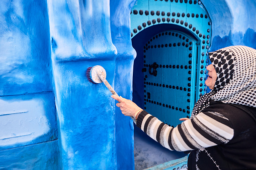 Moroccan woman painting walls with blue paint in Chefchaouen, Morocco, North Africa.