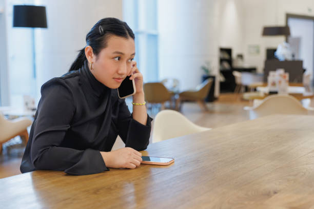 istock Young Asian woman working from hotel lobby, making a call on mobile phone and using e-organizer 2062744256