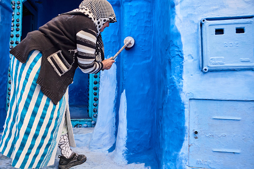 Moroccan woman painting walls with blue paint in Chefchaouen, Morocco, North Africa.