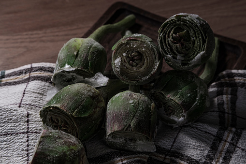 fresh frozen baby artichoke buds raw on kitchen cloth textle, wooden board, dark rustic colors, ready to cook
