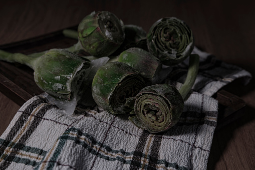 fresh frozen baby artichoke buds raw on kitchen cloth textle, wooden board, dark rustic colors, ready to cook