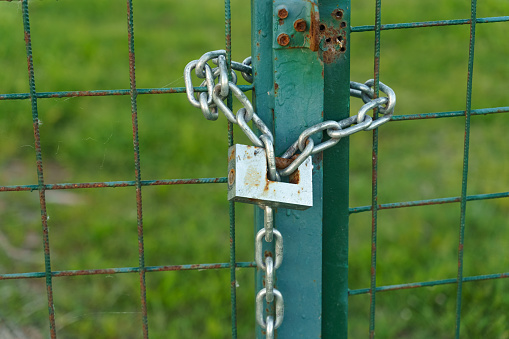 A green gate stands closed with a metal chain securing it shut. The chain is attached to the gates latch, ensuring it remains closed.