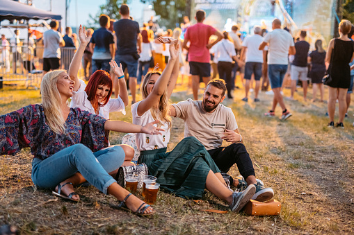 Group of young people sitting on the grass and dancing at the music festival.