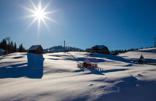 Landscape with a rural household in a mountain village in winter. An isolated house in the countryside on a slope covered with snow