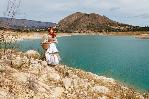 Portrait of a woman dressed as a vintage peasant with the landscape of the Amador reservoir with low water levels due to climate change, Spain