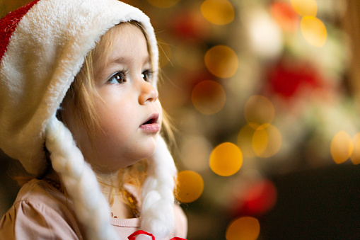 Close-up portrait of a little girl with a Santa hat and Christmas lights. Copy space