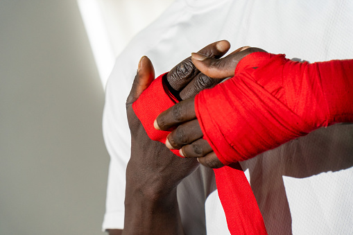 A black Muay Thai fighter carefully wraps his hands, gearing up for battle with determination, in a powerful and inspiring image.