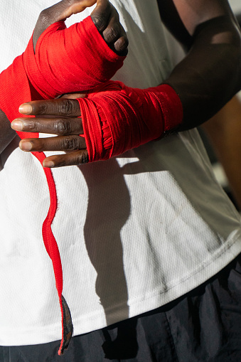 A black Muay Thai fighter carefully wraps his hands, gearing up for battle with determination, in a powerful and inspiring image.