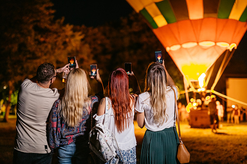 Group of young people taking pictures using smart phone of a hot air balloon at the music festival.