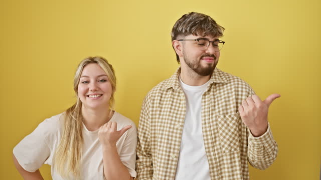 Optimistic, beautiful couple together, standing against isolated yellow background, confidently gesturing thumbs up with open mouths. their smiling faces exude joy, love, and positive vibes.
