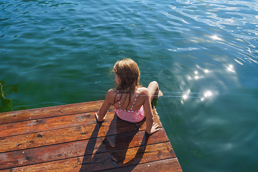 Girl sits on the wooden jetty with her feet in the water. Enjoy summer vacation.
