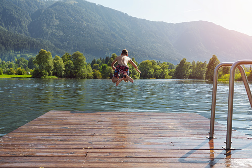 Boy jumping off the dock into the lake - a fun summer vacation.