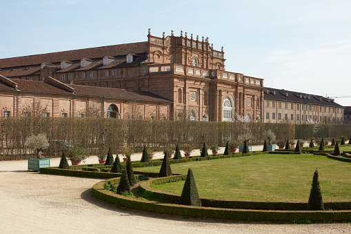 Venaria Reale, Italy - March 29 , 2023: Reggia di Venaria castle architecture and park with pyramidal hedges in spring sunlight