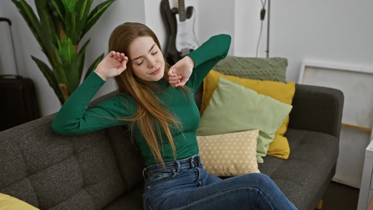 Peaceful portrait of a beautiful young blonde woman wearing a cozy sweater, eyes closed, hands posed in a sleepy gesture, immersed in happy dreams at home. a symbolic picture of rest and relaxation.