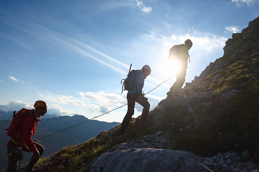 Three mountain climbers silhouettes against a blue sky with sun.