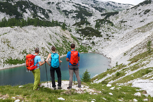 Drone view; Three young adults on top of rock arms open above alpine lake in the Alps having fun and enjoying summer hiking in fresh environment; 3 friends; People outdoor activities concept