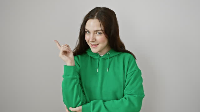 Cheerful young woman in hoodie confidently presenting, pointing finger off to the side, alight with a radiant smile. perfect for product showcase, isolated on a clear white backdrop.