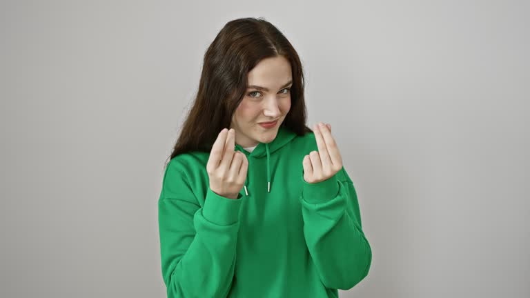 Confident young woman model wearing sweatshirt standing, doing sneaky money gesture with hand, gesturing salary payment concept, isolated on white background, bossing business success