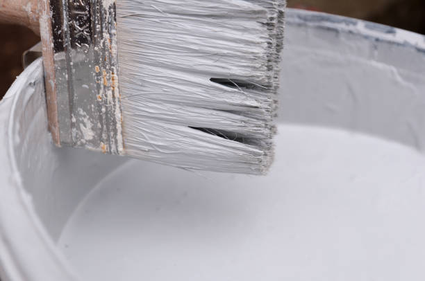 A Brush with gray paint put on the paint bucket