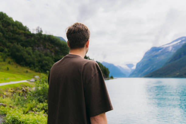 Rear view of a man traveler admiring crystal moue lake Lovatnet with view of green mountain peaks and glacier in Jostedalbreen National park, Norway