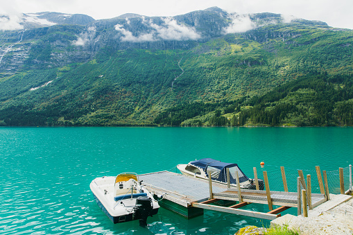 Scenic view of two boats on the pier at turquoise coloured glacial lake Lovatnet surrounded by beautiful summer mountain peaks in Western Norway, Scandinavia