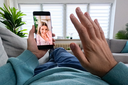 Young man having a video call with a female friend while lying on the sofa in the living room at home. His POV.