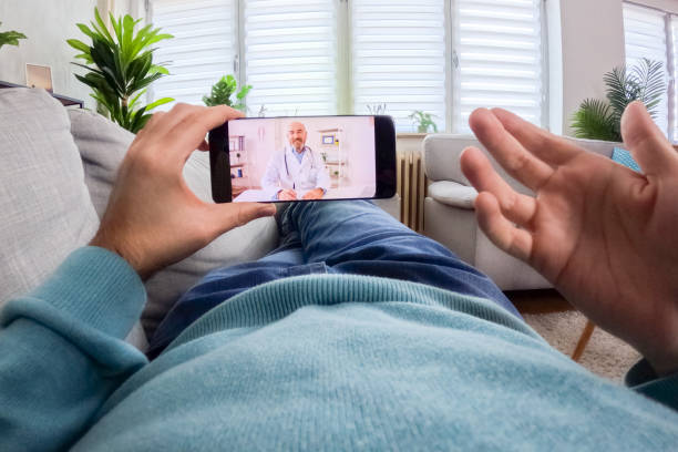 istock Young Man Having A Doctor's Appointment Online Using Smart Phone On The Sofa At Home 2062967421