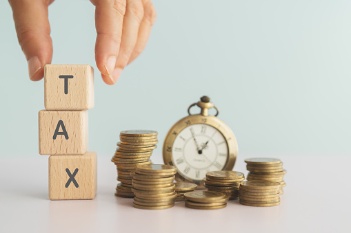 hand completed stack of wooden cube blocks with TAX text and blurred coins, vintage clock