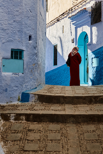 Street with back view of woman wearing traditional clothing in the blue city of Chefchaouen, Morocco, North Africa.
