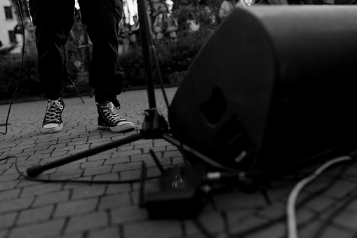 A black and white image capturing the ground view of a musician sneakers, microphone stand, and speaker on a paved surface, evoking the raw energy of street performance