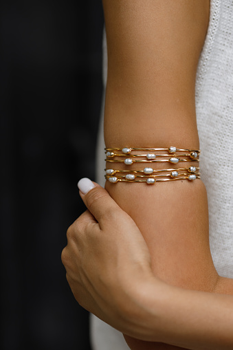 A close-up shot captures the elegance of a gold bracelet, intricately designed and adorned with pearls, gracefully wrapped around a woman wrist. The gleaming jewelry complements the soft glow of her skin