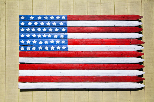 Rustic American flag painted on weathered wooden planks against cream-colored siding. Evokes patriotism and vintage Americana. Empire, Michigan.