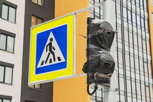 A pedestrian crossing sign is installed on a pole next to a non-working traffic light