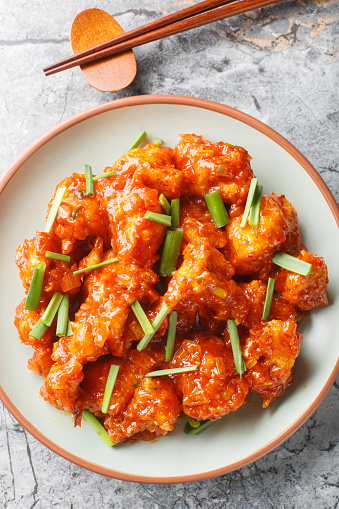 Gobi Manchurian is an Indo-Chinese appetizer crispy and crunchy fried cauliflower coated in a sweet, tangy, umami chili sauce closeup on the plate on the table. Vertical top view from above