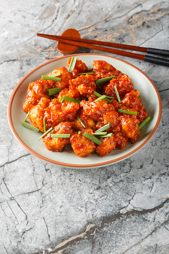 Gobi Manchurian is an Indo-Chinese appetizer crispy and crunchy fried cauliflower coated in a sweet, tangy, umami chili sauce closeup on the plate on the table. Vertical